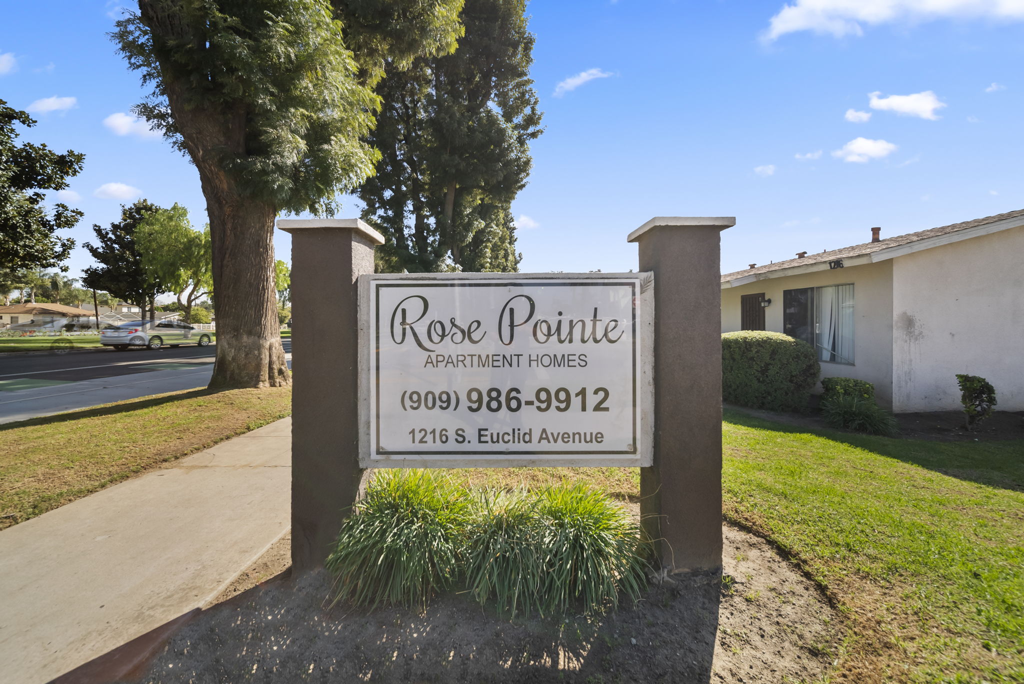 A sign for Rose Pointe Apartment Homes stands in front of a tree.